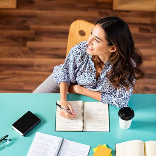Smiling latin girl looking away while studying. Portrait of pensive college student looking away while studying alone at library. Young thinking woman taking notes at university.