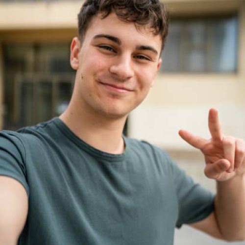 One man young adult caucasian teenager stand outdoor posing self portrait selfie looking to the camera happy confident wear shirt casual real person copy space ugc user generated content
